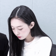 a woman with long black hair and a white shirt is looking down .