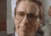a man wearing glasses and a suit is smiling .
