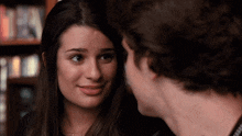 a man and a woman are looking at each other with a bookshelf in the background