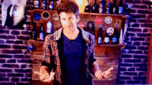 a man in a plaid shirt is standing in front of a brick wall with beer bottles on shelves behind him