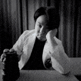 a black and white photo of a person sitting at a table holding a camera lens