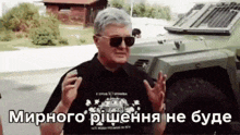 a man wearing sunglasses is standing in front of a vehicle .