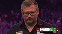 a man wearing glasses stands in front of a screen that says first to 16 wade and rock