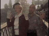 a man and a woman standing on a bridge waving their hands