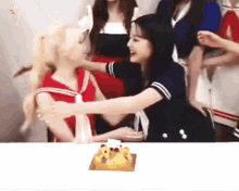 a group of girls are standing around a table with a cake in the middle