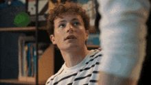 a young man with curly hair is wearing a striped shirt and looking up .