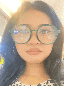 a woman wearing a pair of green glasses with a blue sticker on the lens