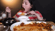 a woman is eating a plate of food with chopsticks and a spoon
