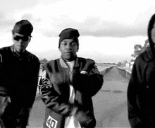 a black and white photo of three men standing next to each other on a road .