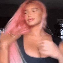 a woman with pink hair is wearing a black tank top and holding her hair .