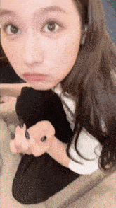 a woman with long black nails is sitting on a couch looking at the camera
