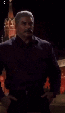 a man with a mustache is standing with his hands on his hips in front of a red tower