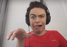 a young man wearing headphones and a red shirt that says atznx makes a funny face