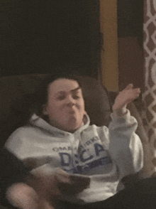 a woman wearing a hoodie that says dca on it is sitting in a chair