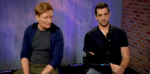 two men sit next to each other in front of a brick wall .