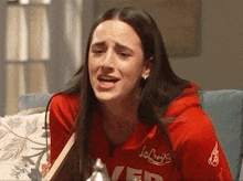 a woman in a red sweatshirt is sitting on a couch with her mouth open .