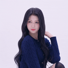 a woman with long black hair wearing a blue sweater looks at the camera