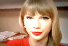 taylor swift is wearing a red shirt and red lipstick and looking at the camera .