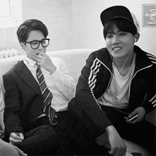 a man in a suit and tie is sitting on a couch next to another man