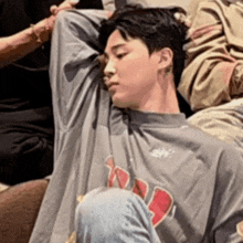 a man in a gray shirt is sitting on a couch with his arms over his head .