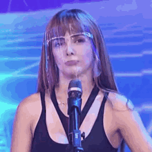 a woman is wearing a face shield and standing in front of a microphone .