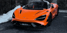 an orange sports car is parked in front of a snow covered fence
