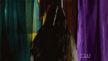 a woman with dreadlocks is holding a sword in front of a curtain with the letters cw on it .