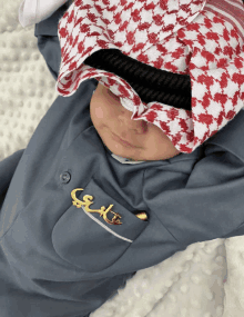 a baby wearing a keffiyeh and a brooch that says ' s ' on it