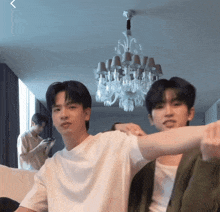 two young men are sitting in front of a chandelier