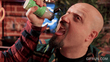 a bald man with a beard is drinking from a bottle with the website gifrun.com in the corner