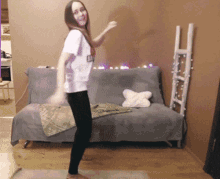 a woman is dancing in front of a couch with a ladder behind her