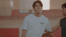 a man in a white t-shirt is holding a basketball in a gym .