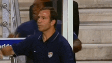 a man in a blue shirt is standing in front of a glass door and talking on a cell phone .