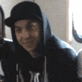 a man wearing a hooded sweatshirt and a hat is smiling .