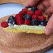 a person is holding a slice of pie with raspberries and blueberries