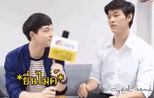 two young men are sitting on a couch talking to each other while one of them holds a microphone .