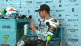 a man wearing a leopard racing jersey sits in front of a wall