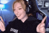 a woman wearing headphones and a hoodie that says nirvana is smiling and making a peace sign .