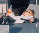 a little girl wearing sunglasses is laying in a chair holding a bottle of orange juice .