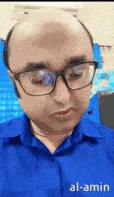 a bald man wearing glasses and a blue shirt with al-amin written on the bottom right