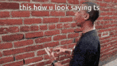 a man standing in front of a brick wall with the words this how u look saying ts