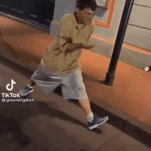a man in a yellow shirt and grey shorts is walking down a sidewalk .