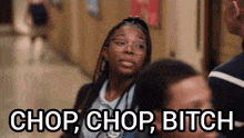 a girl with glasses is standing in a hallway with the words chop chop bitch above her