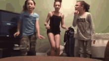 three young girls are dancing in a living room in front of a flat screen tv .