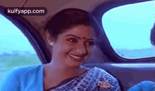 a woman in a blue saree is sitting in the back seat of a car and smiling .