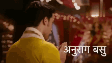 a man in a yellow shirt is praying in front of a blurred background and the words anurag basu are visible