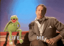 kermit the frog is sitting on a couch next to a man in a suit and tie .