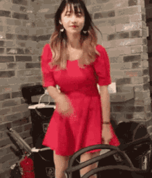 a woman in a red dress is standing in front of a brick wall ..