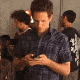 a man in a blue plaid shirt is looking at his phone