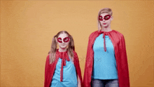 a mother and daughter are dressed in superhero costumes and masks and holding hands .